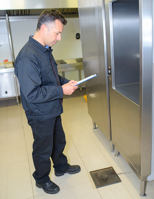 A male pest control technician at a commercial kitchen with a clipboard