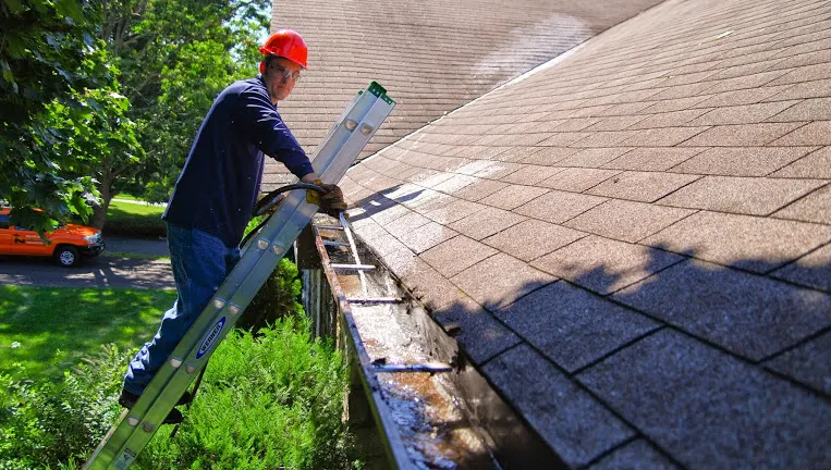 man on ladder cleaning gutter
